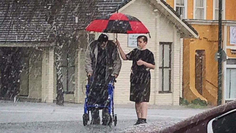 Asystent chroniący seniora parasolem podczas wyjścia w deszczu